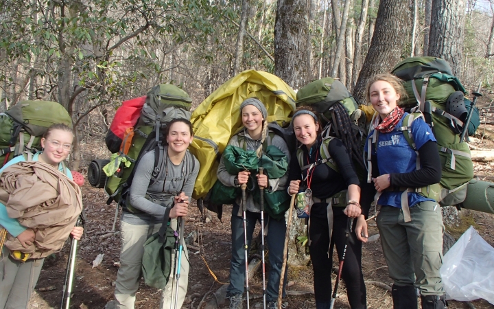a group of people wearing backpacks pose for a photo in a wooded area
